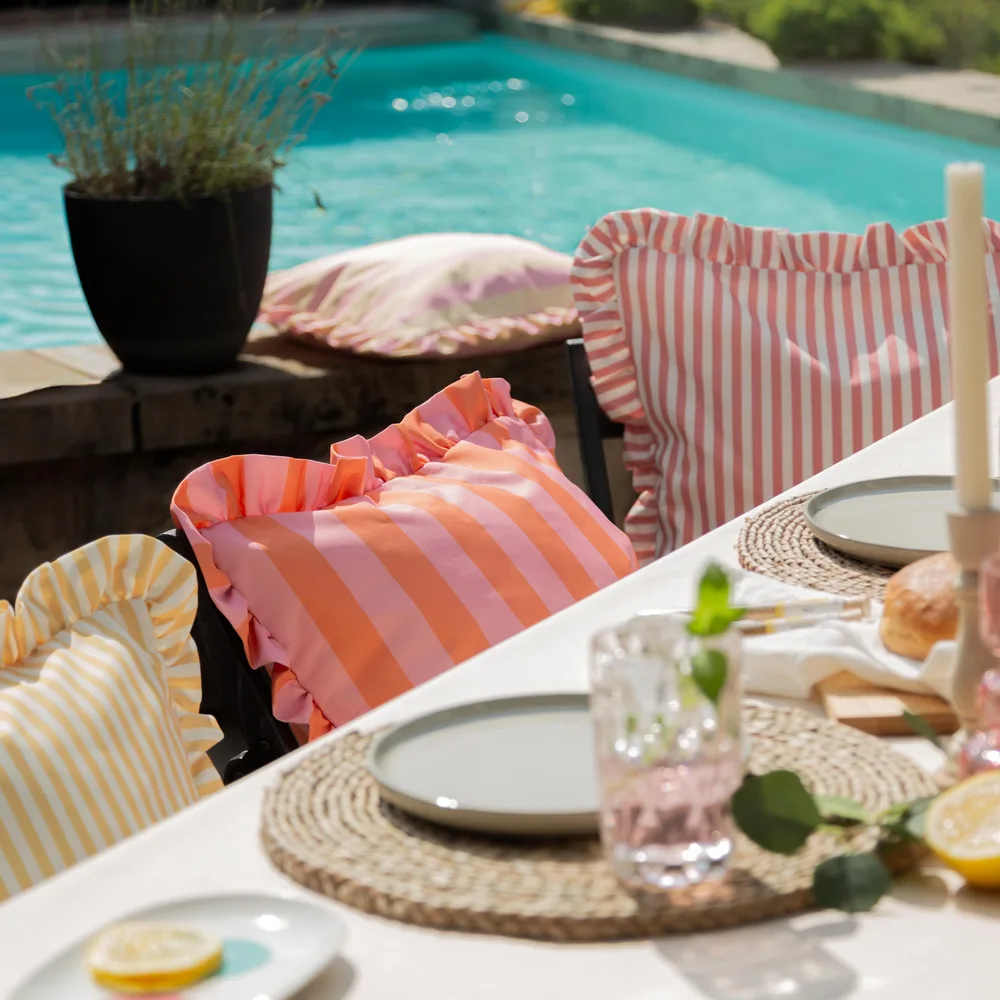 Gedeckter Tisch am Pool mit gestreiften Rüschenkissen, geflochtenen Tischsets und Zitronen