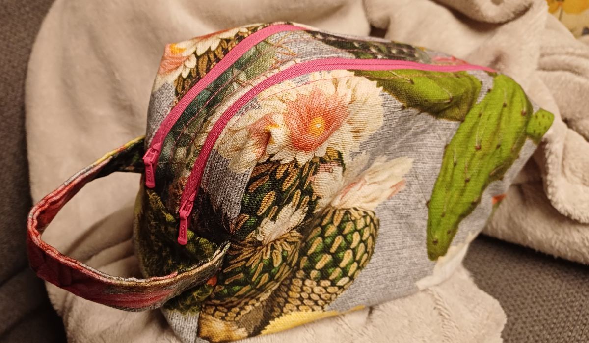 Selbstgenähte Kulturtasche aus Dekostoff mit Kakteen-Digitaldruck auf grauem Grund, zwei pinke Reißverschlüsse und Henkel